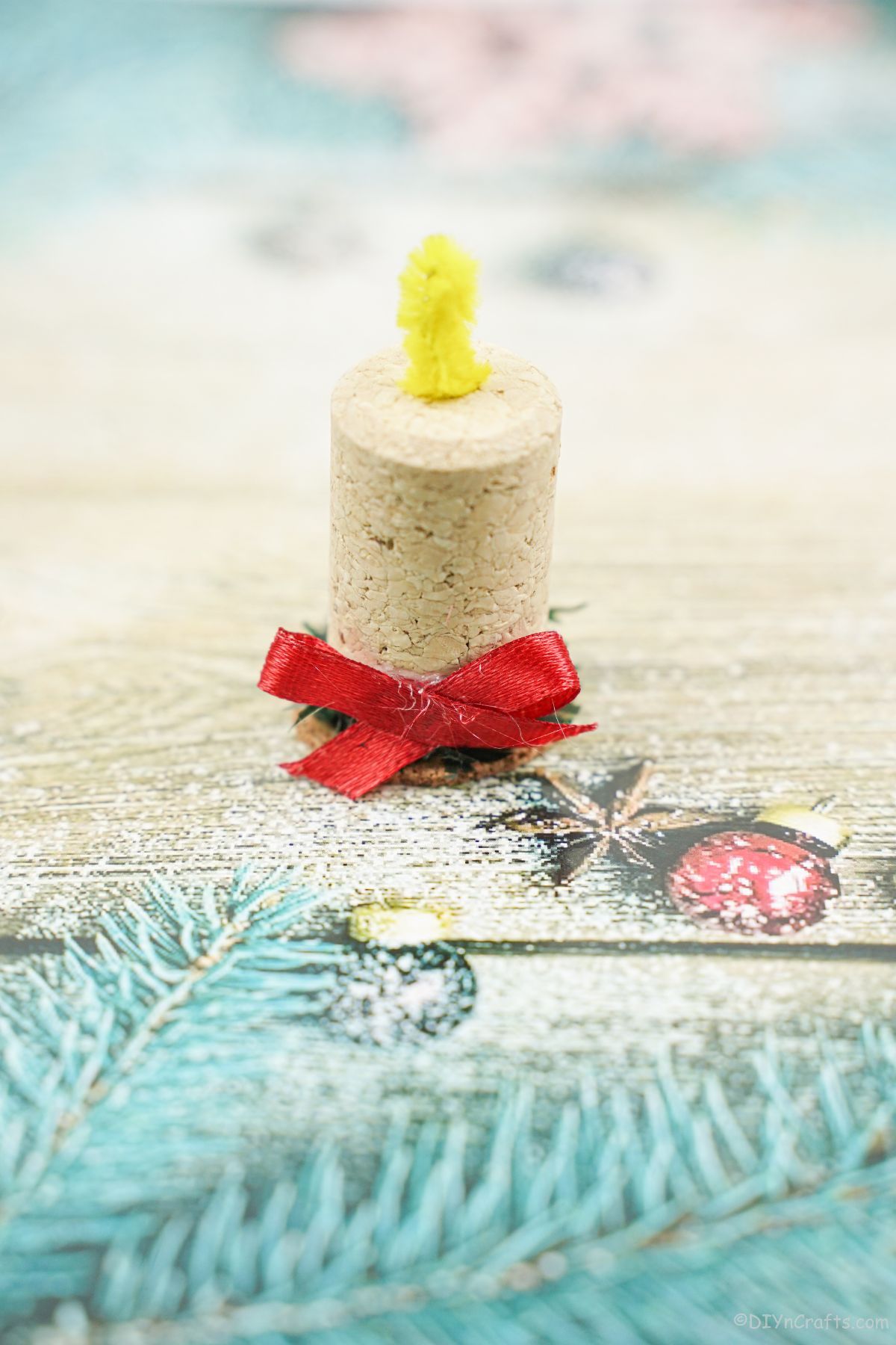 holiday paper that is teal with fake leaves holding wine cork candle
