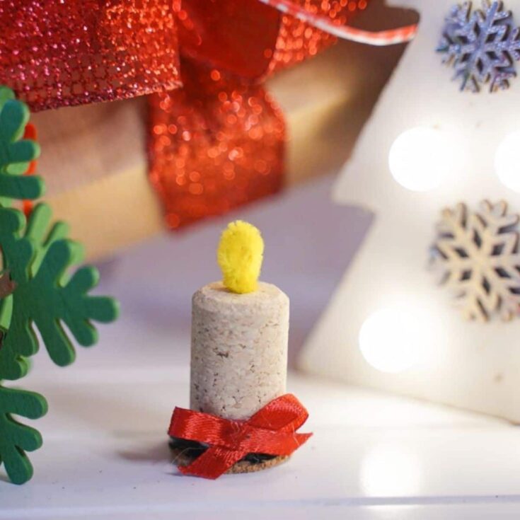 wine cork candle on white table with green holiday stems in background