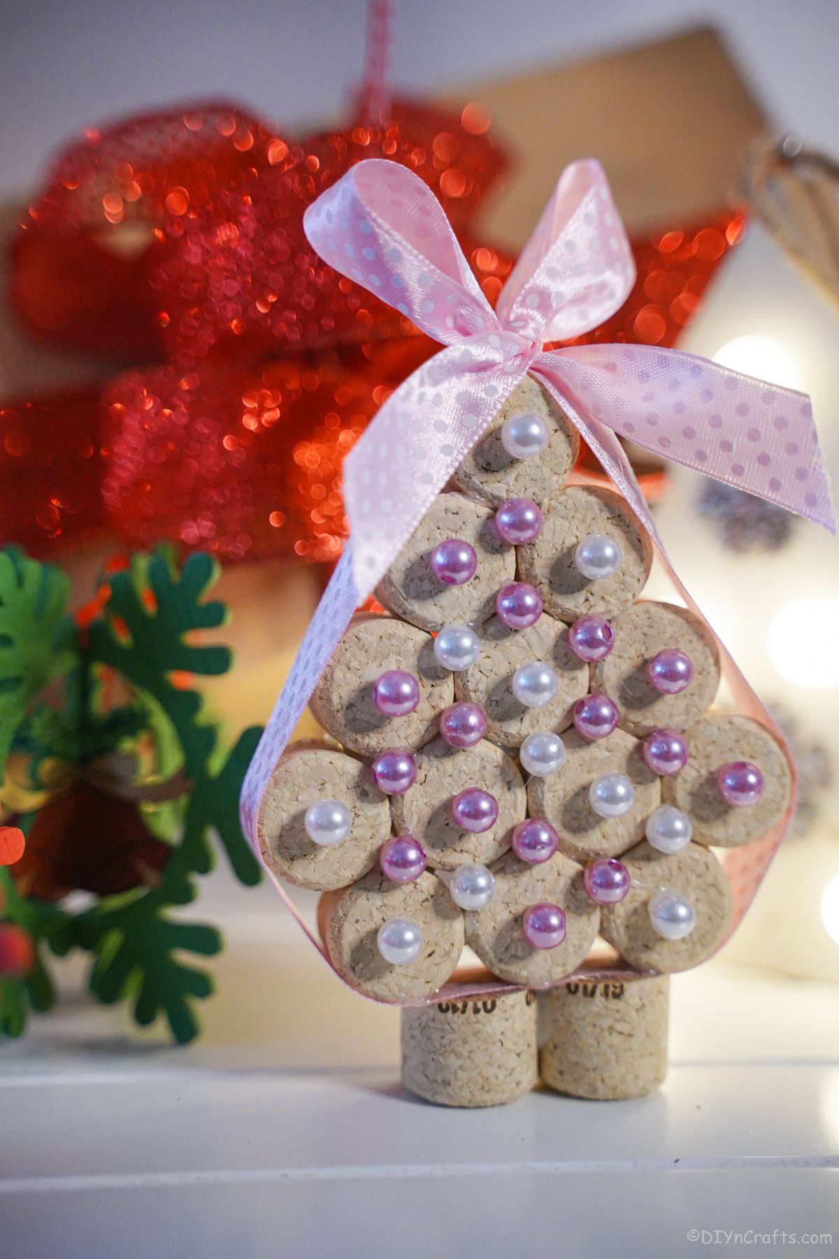 cork mini tree with pink and white beads on white table with red flower in background