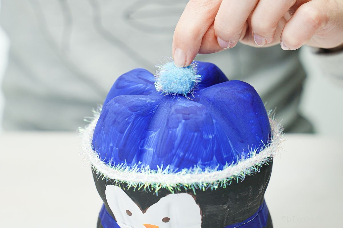 hand holding a blue pom pom on top of the bottle