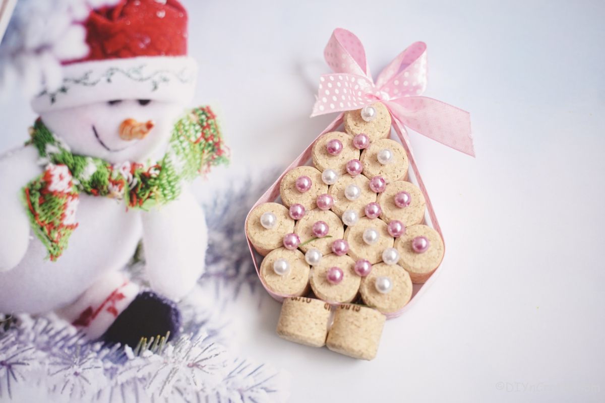 fake mini christmas tree with pink and white beads on white paper with paper snowman