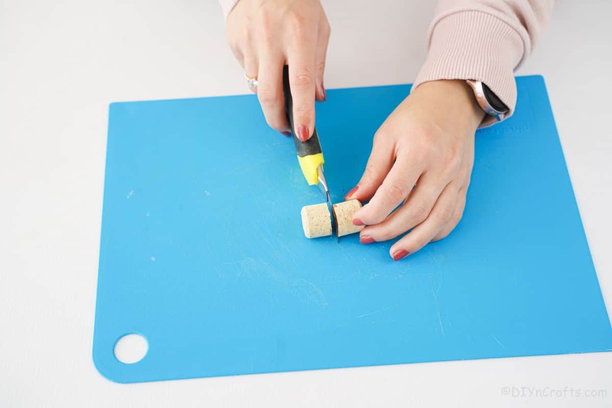 hand cutting cork in half on blue cutting mat