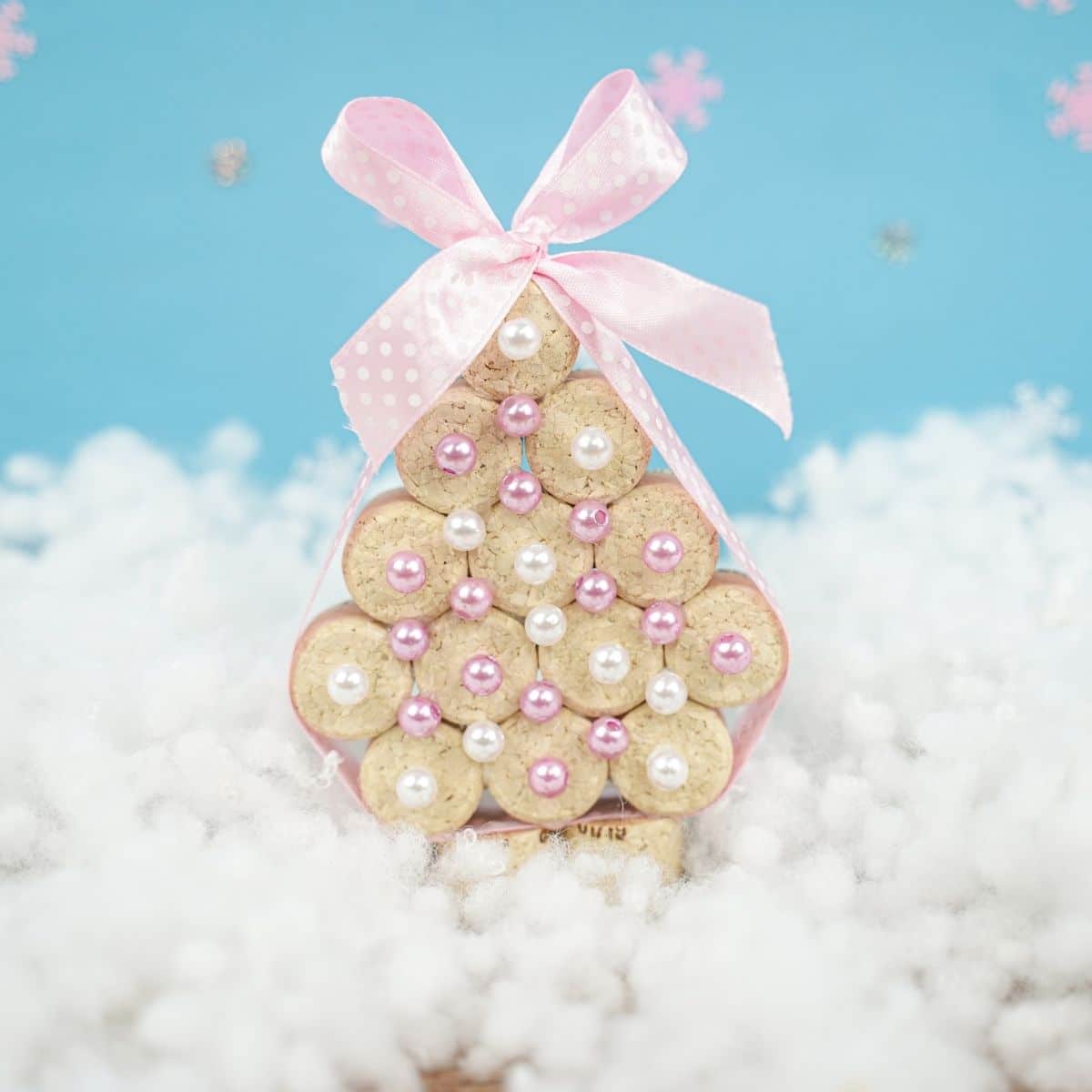 cork tree with pink ribbon and white beads on fake snow with blue background