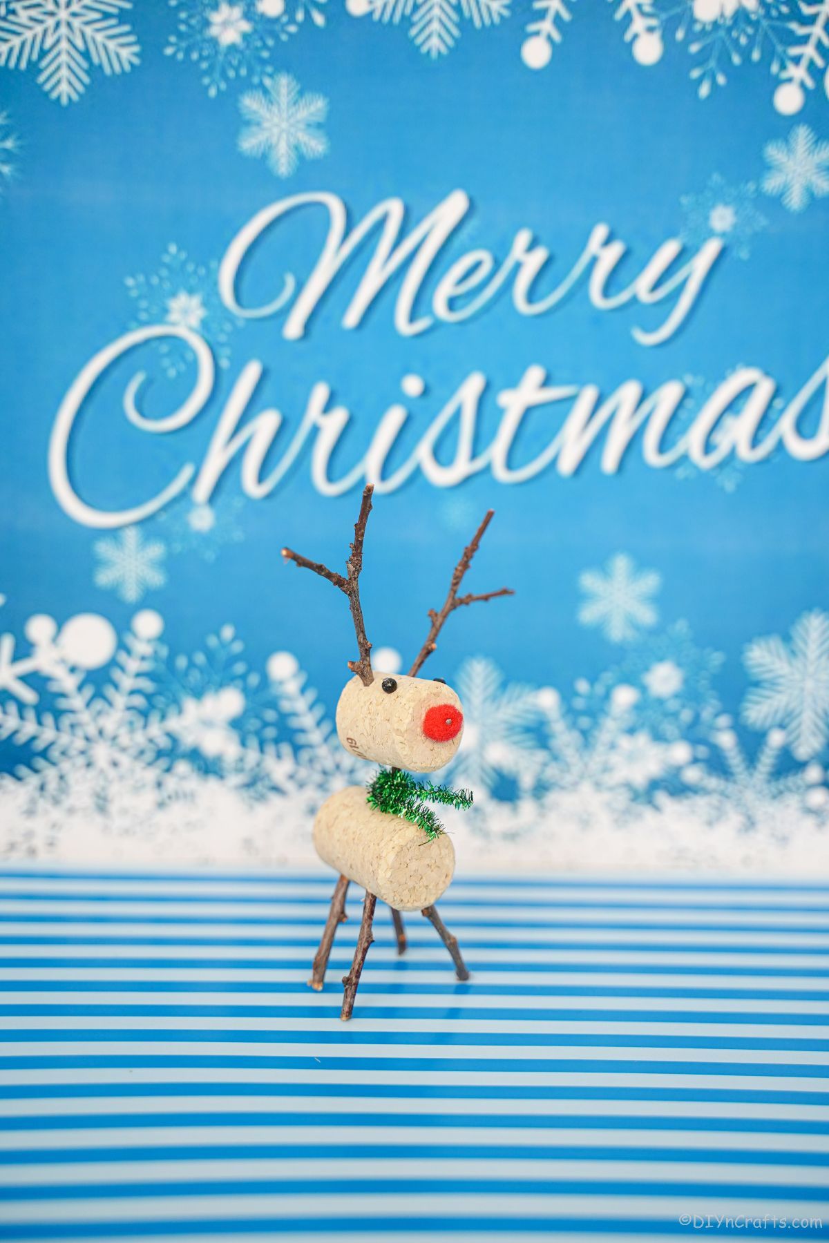 majhni severni jeleni iz plute na modro-beli mizi z belim veselim božičem v ozadju