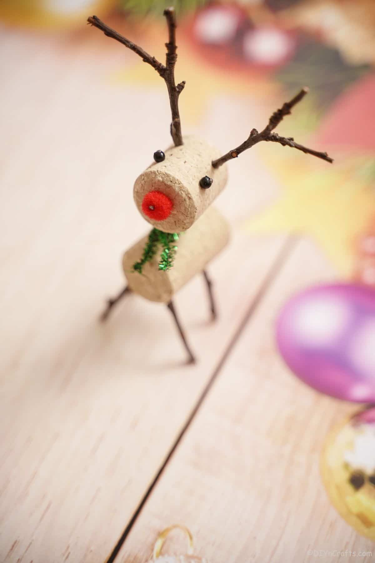 red nosed wine cork reindeer with twig antlers on holiday themed paper