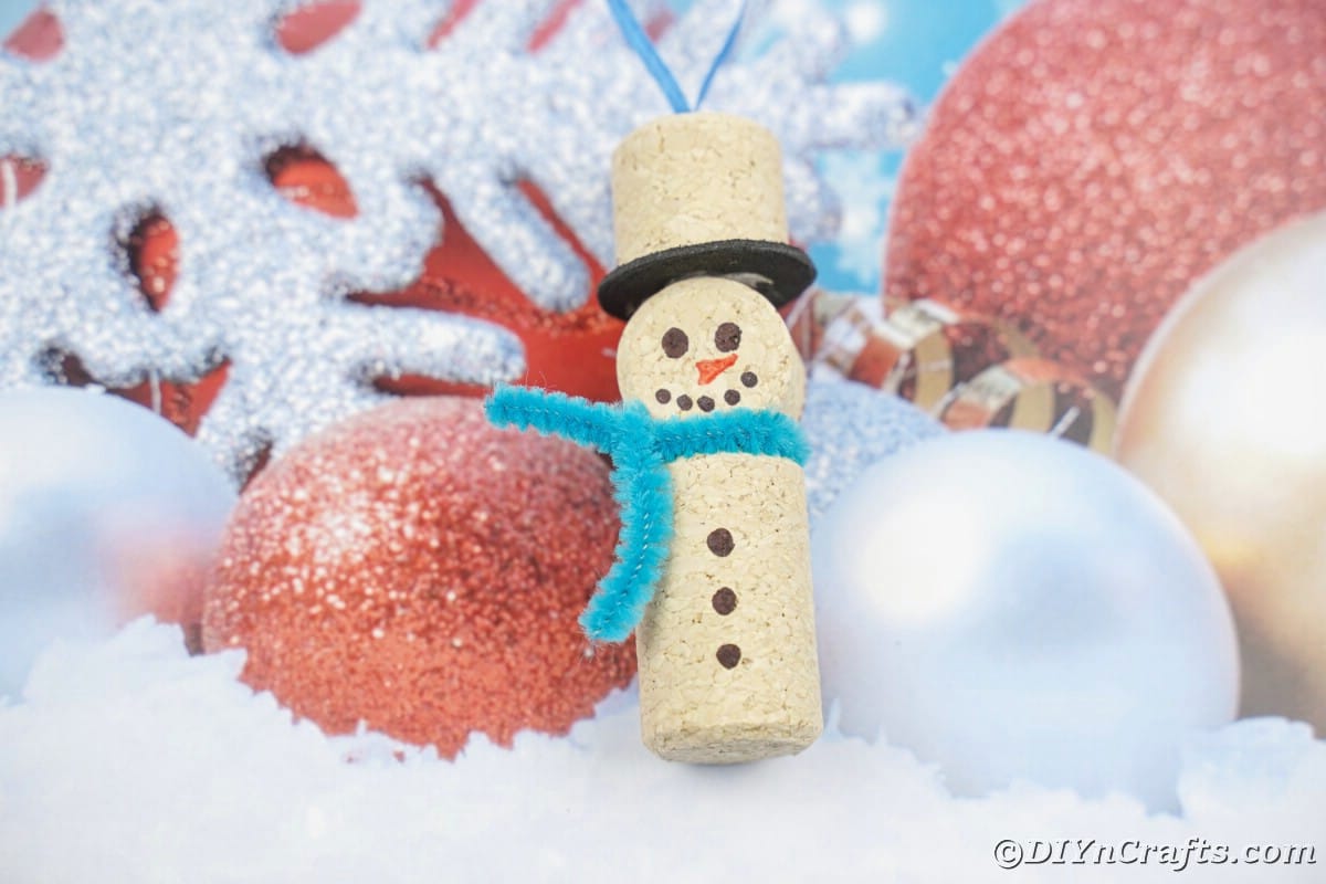 wine cork snowman ornament with blue pipe cleaner scarf on fake ornament paper