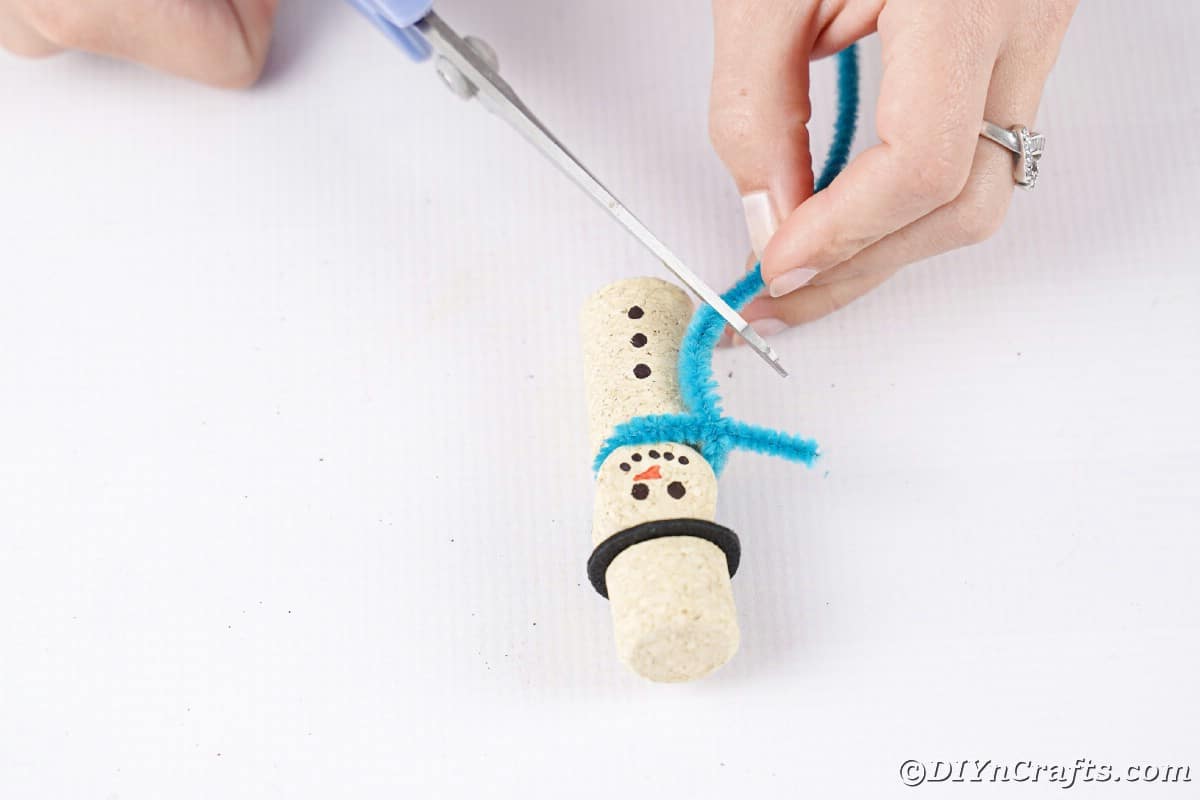 hand trimming blue pipe cleaner off bottom of wine cork snowman
