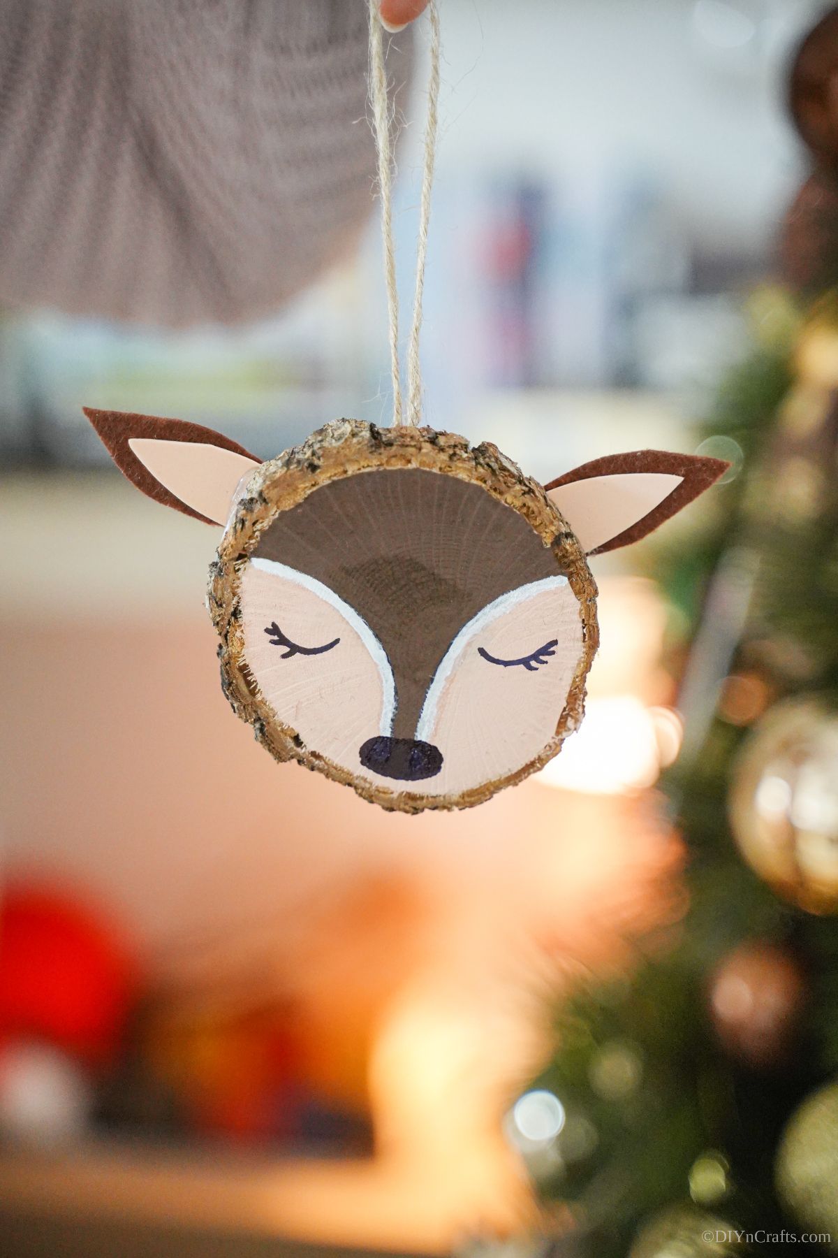 painted wood slice ornament being held in front of tree