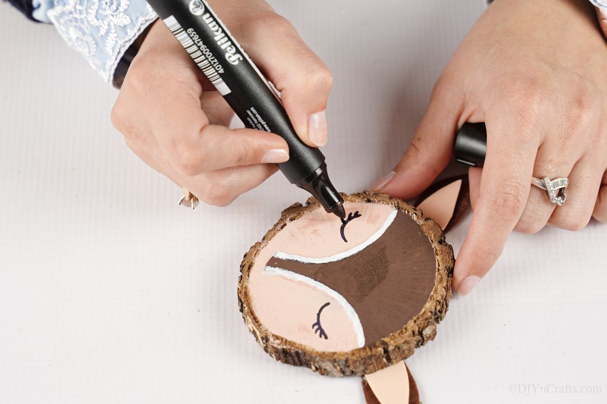 marker drawing eyes on reindeer face of wood slice ornament