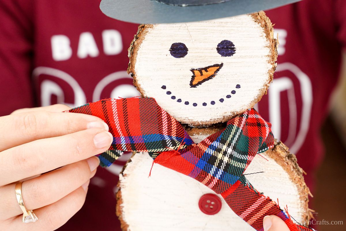 hand adding plaid fabric around wood slice snowman