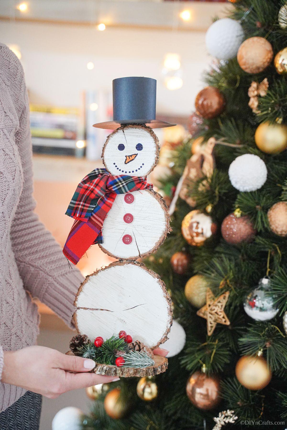 lady holding wood slice snowman in front of christmas tree