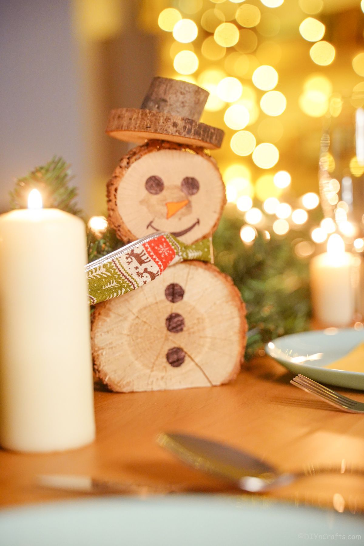 holiday place setting with white candle next to wood slice snowman