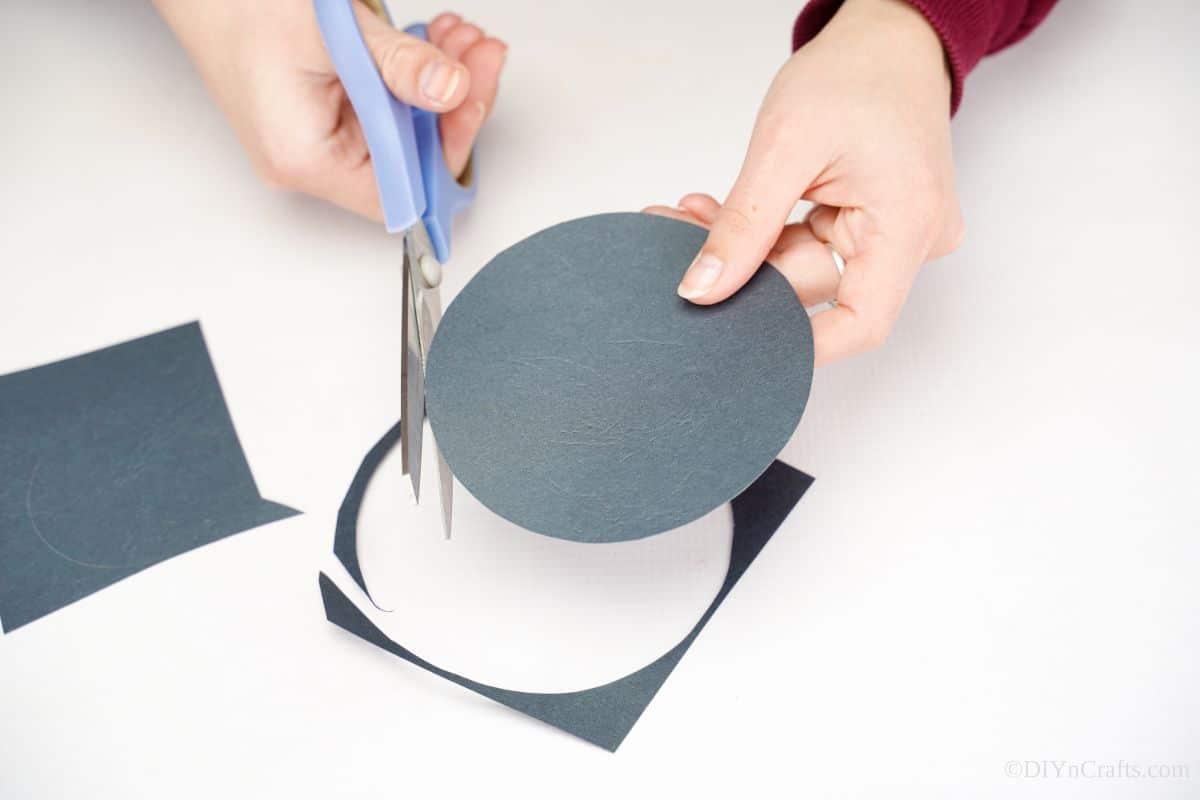blue scissors cutting black circle from paper
