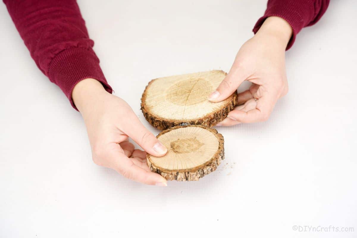 hands holding wood slices together over white table