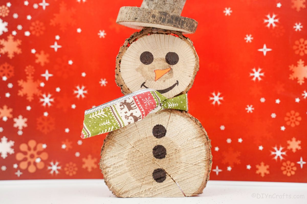 red holiday snowflake background behind wood slice snowman