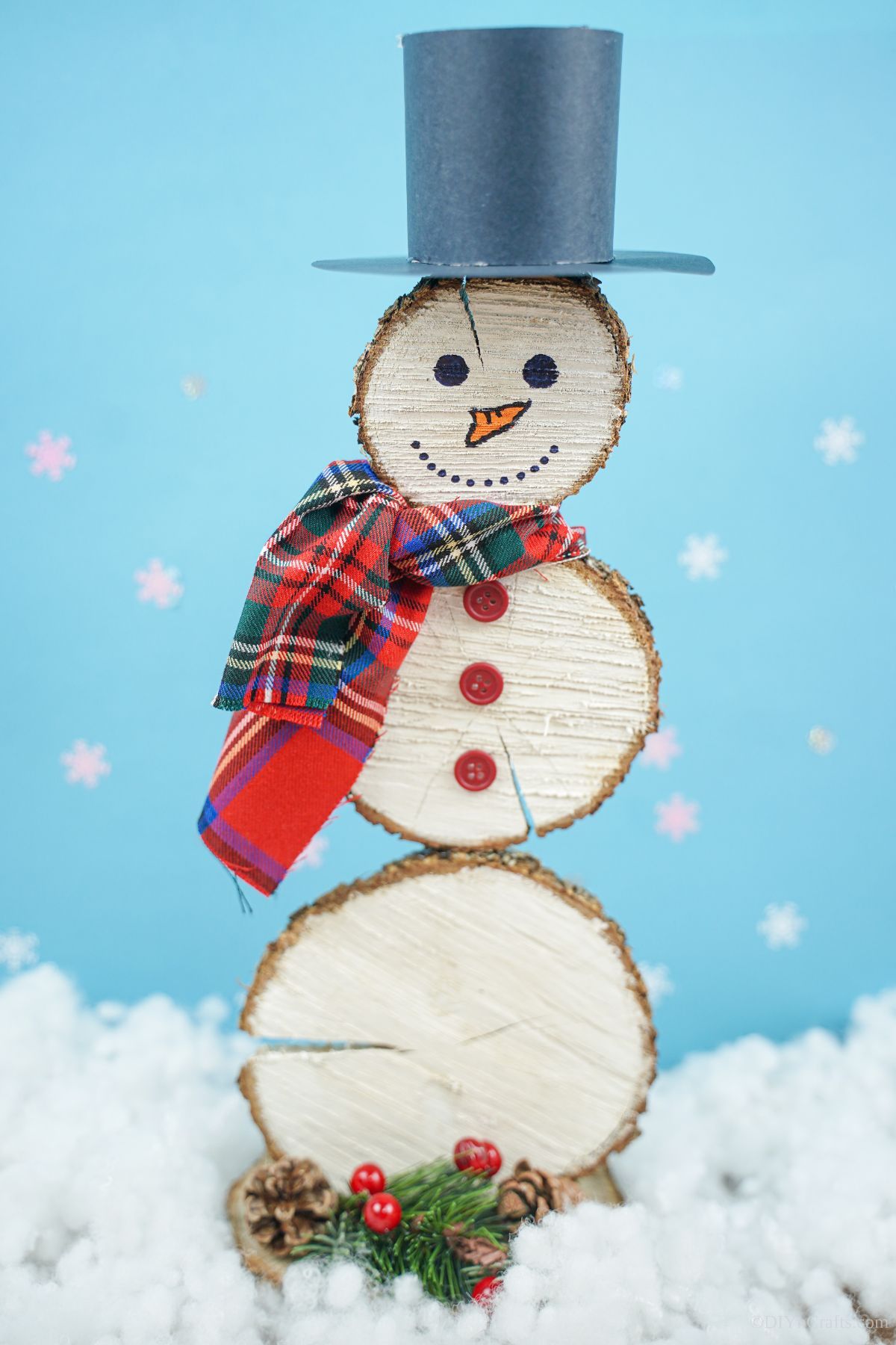 wood slice snowman in front of light blue background with fake snow