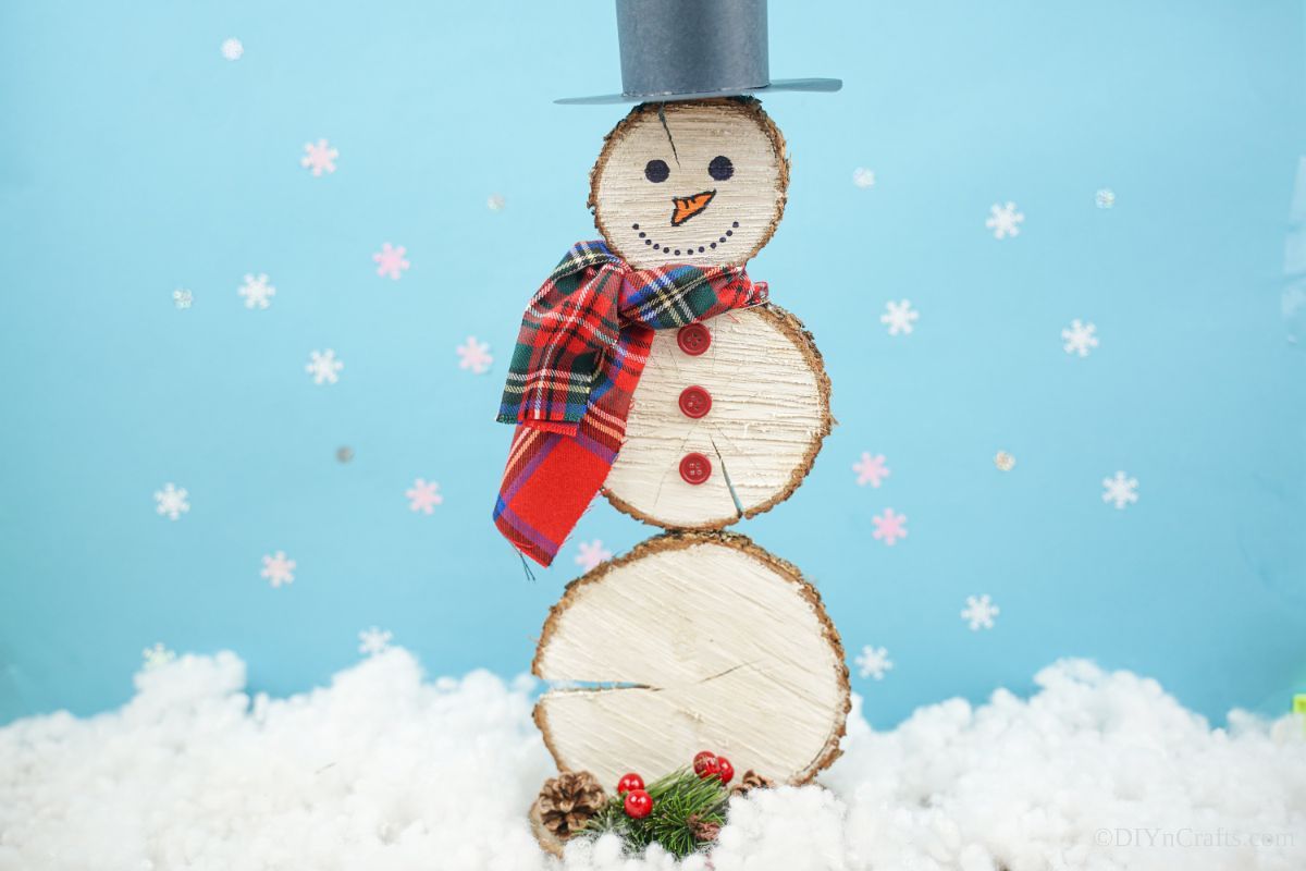 snowman made of wood slices on fake snow in front of blue background