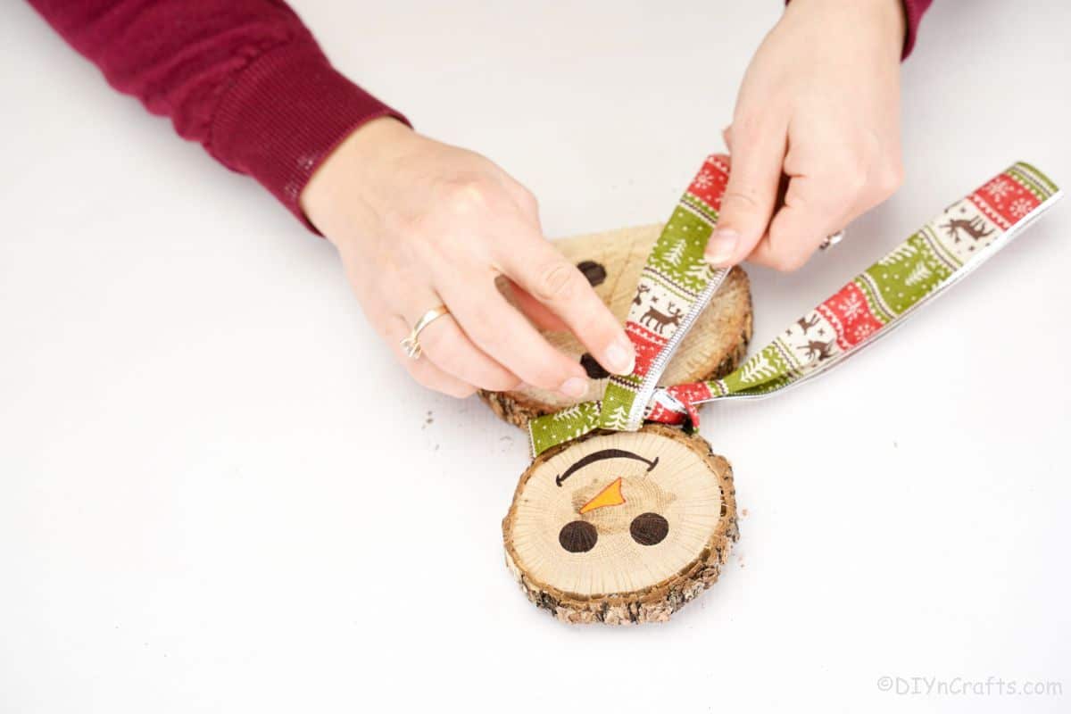 finger holding holiday ribbon on wooden snowman