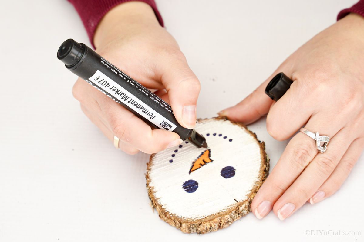 hand using black marker to trace around outside of orange nose on wood slice