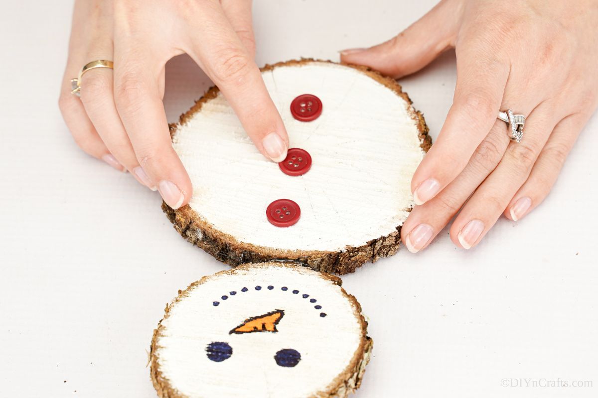 hand gluing red buttons on middle of wood snowman