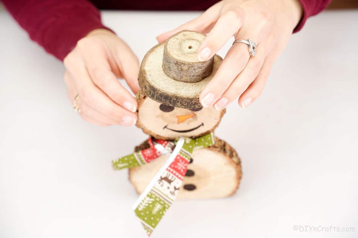 hand holding wooden hat on top of wood slice snowman