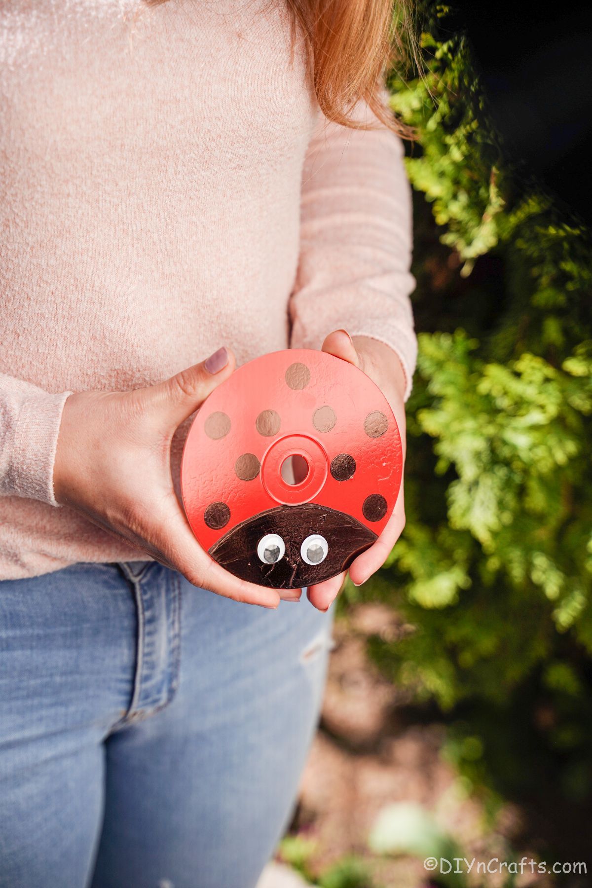 lady in pink and jeans holding a painted cd that looks like a ladybug