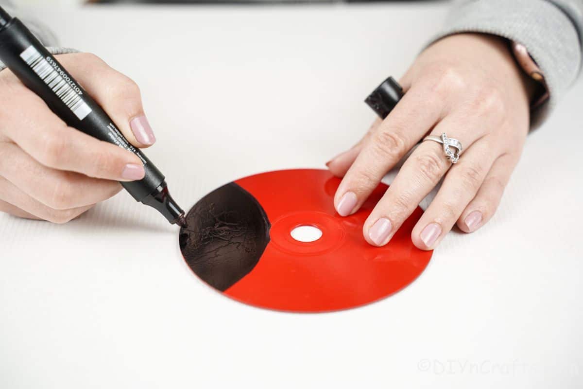 roko, ki drži črni marker obarvanje na delu rdečega CD-ja