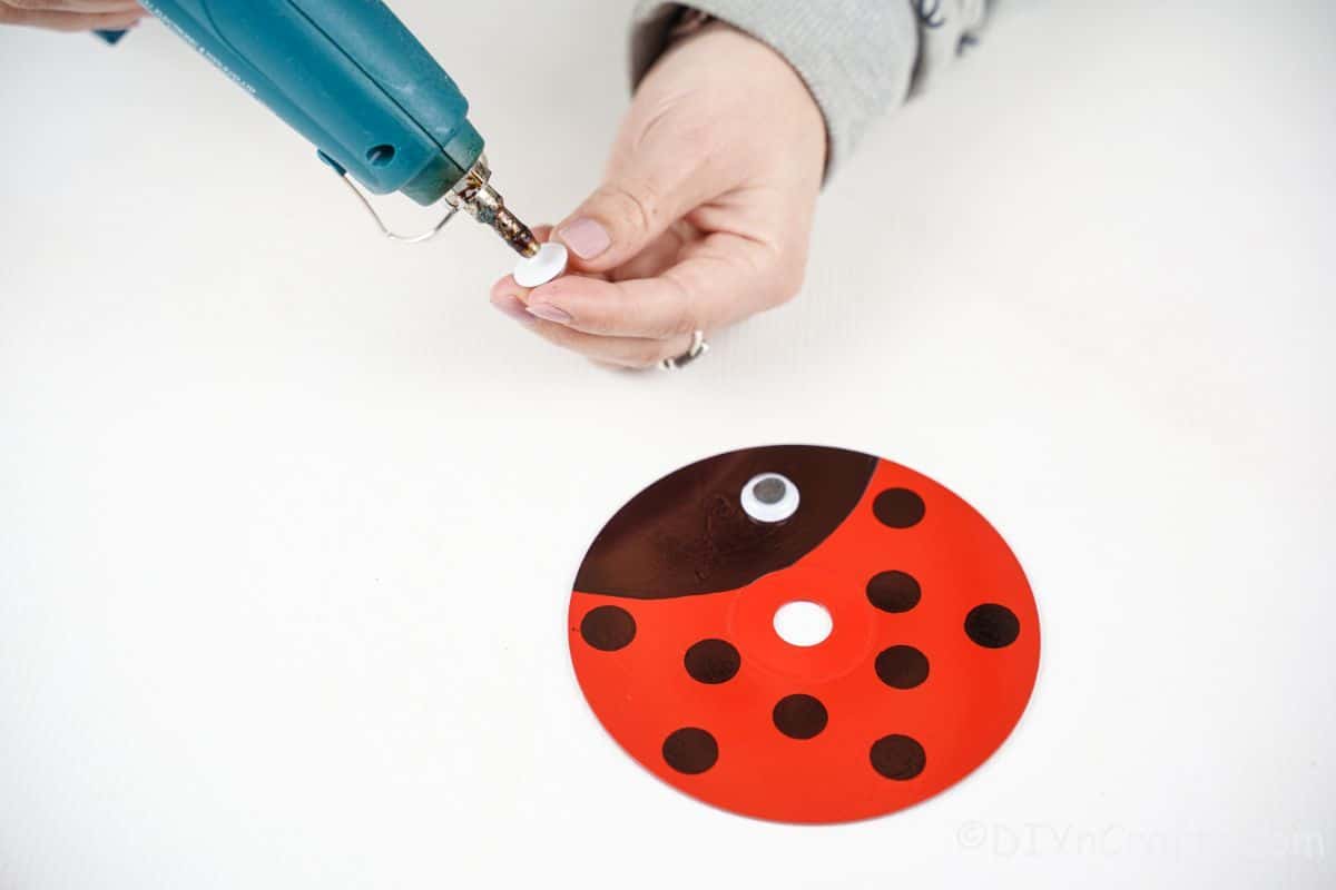 hand holding glue gun over cd that is painted like a ladybug