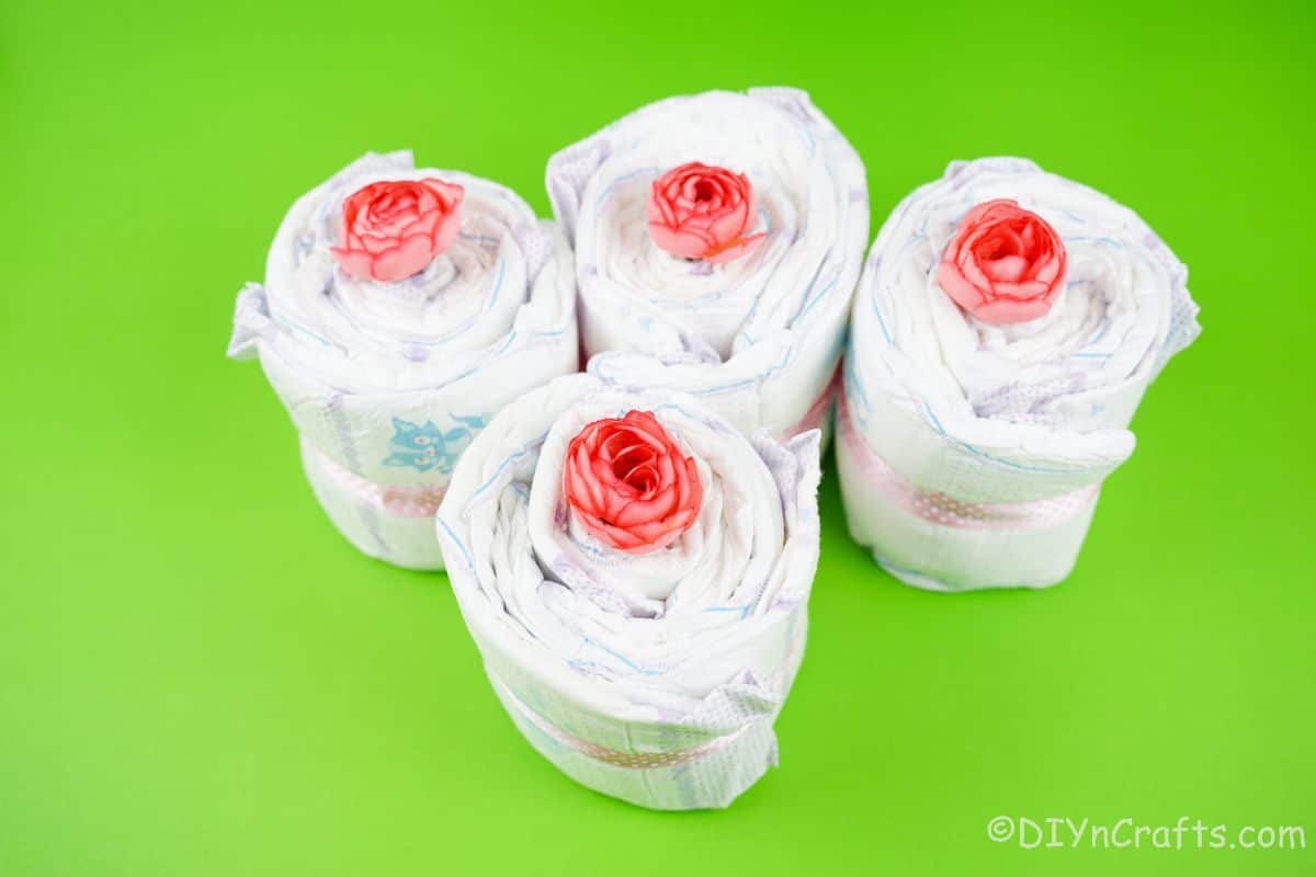 four diaper rolls with fake flowers in the center on green table