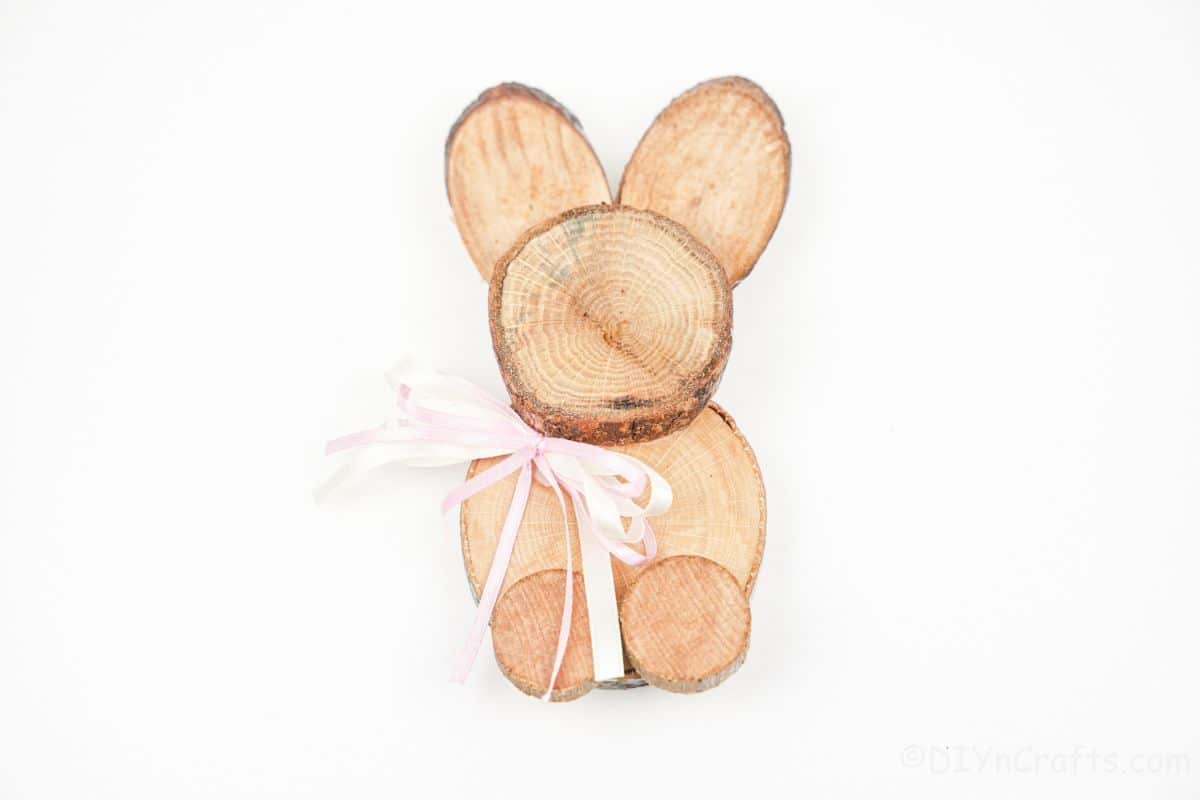 pink ribbon on neck of wood slice bunny sitting on white table