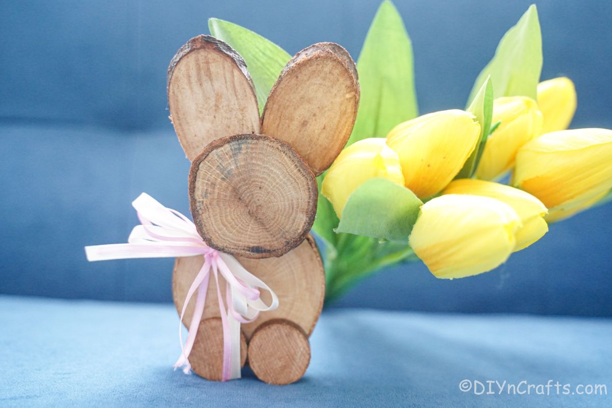 yellow flowers behind wood slice bunny on couch