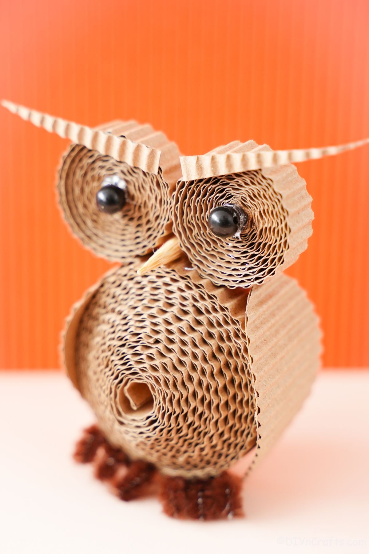 cardboard owl with black bead eyes in front of orange background