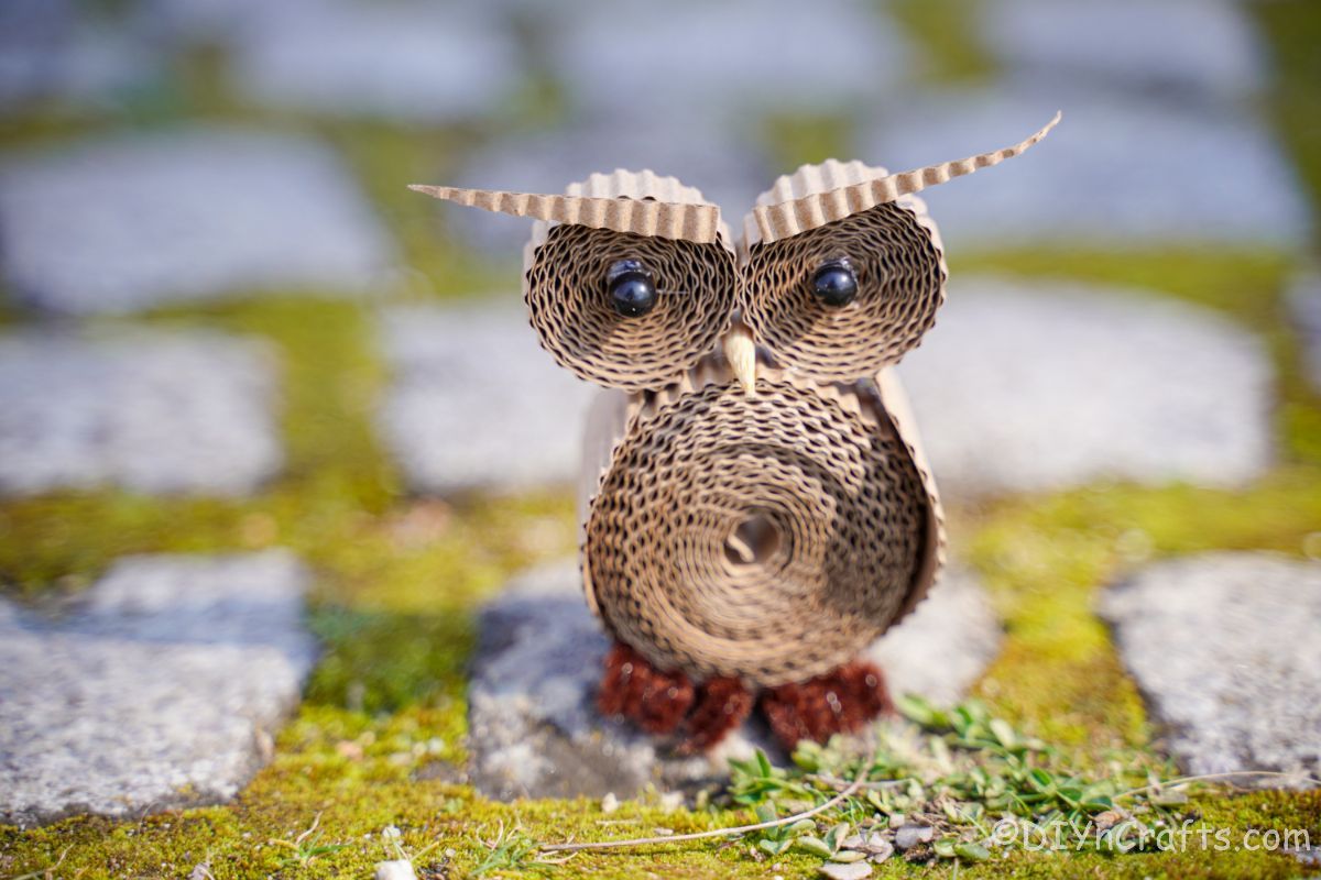 rolld cardboard owl miniature on grass and rock path