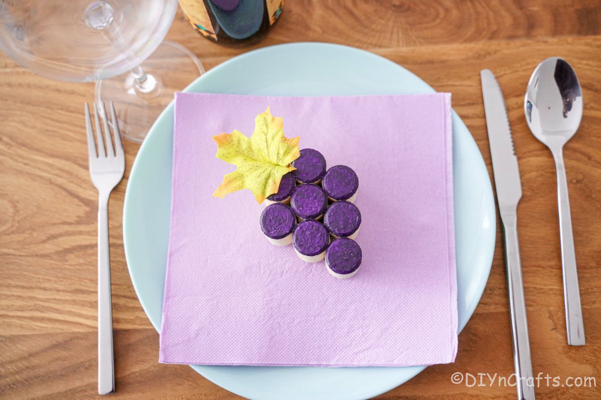eround white plate with lavender napkin on top holding a wine cork grape cluster