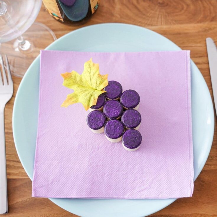 round white plate with lavender napkin on top holding a wine cork grape cluster