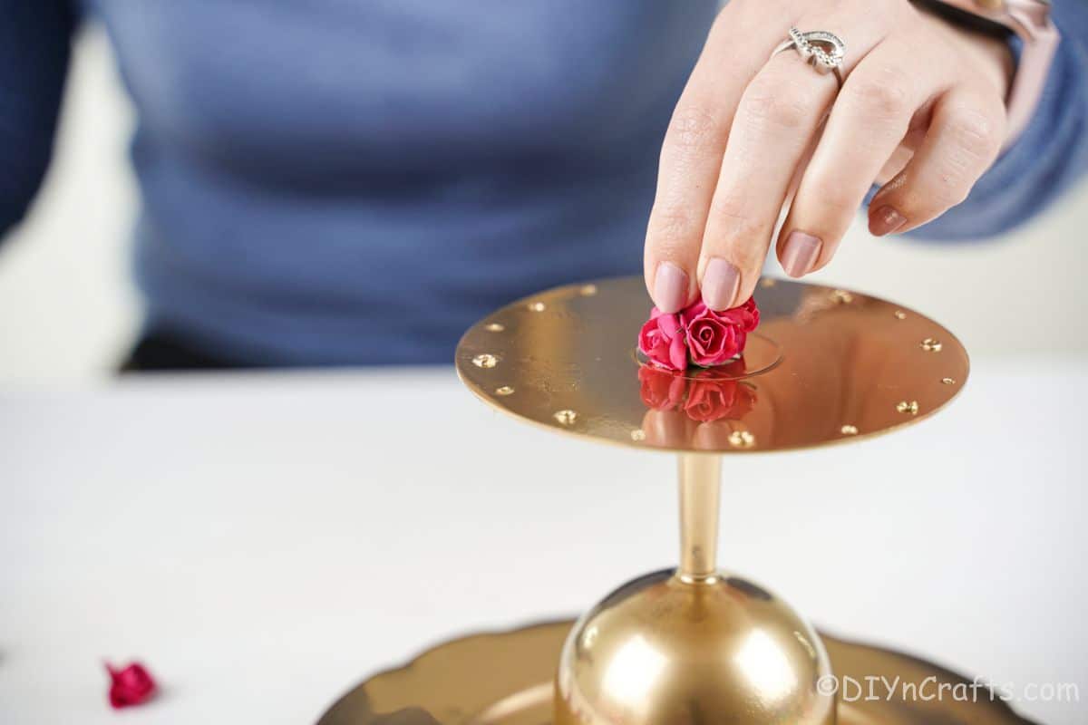 hand holding fake rose on top of gold earring and jewelry holder
