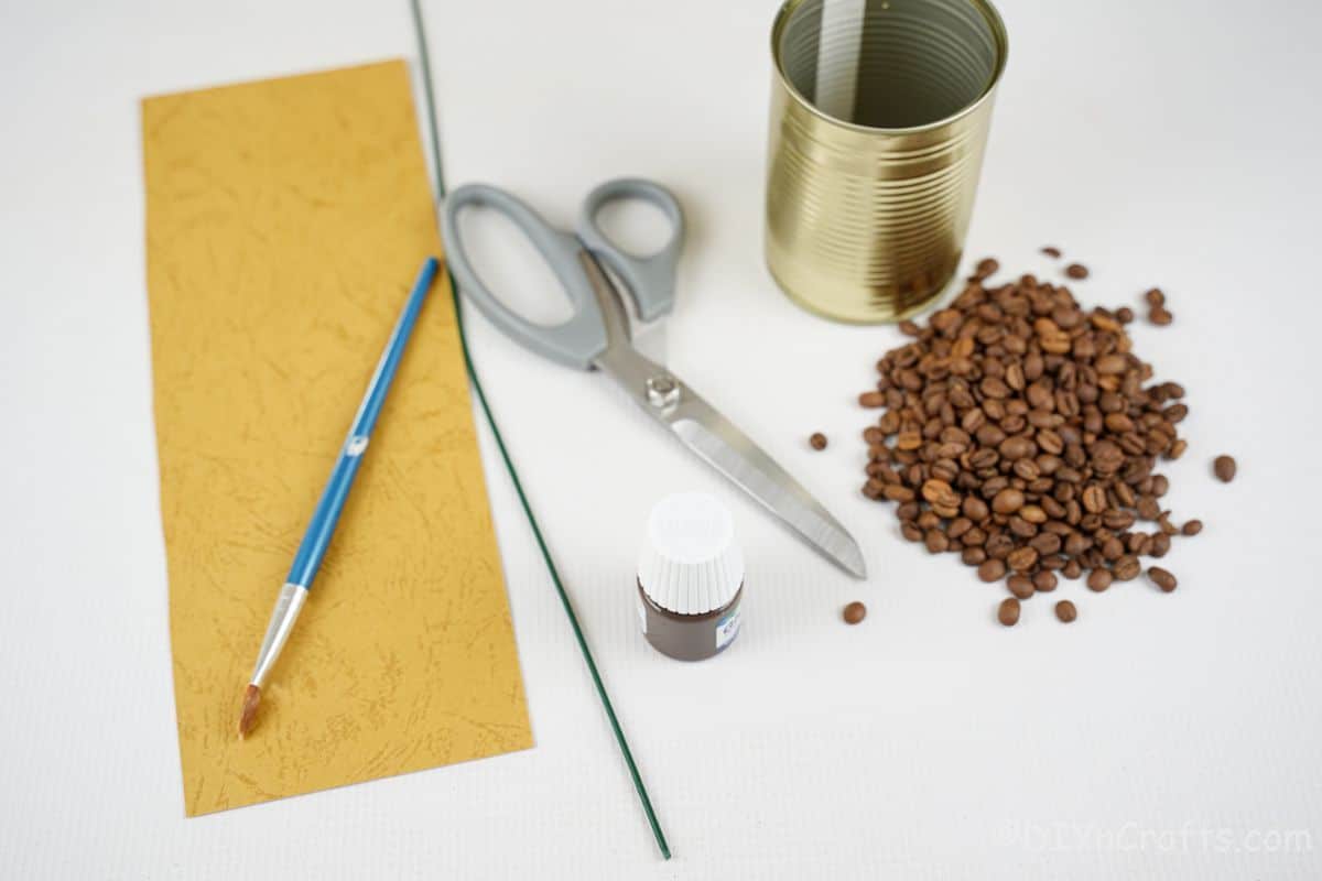 rumeni papirni čopič kavna zrna pločevinka in cvetlična žica na beli mizi