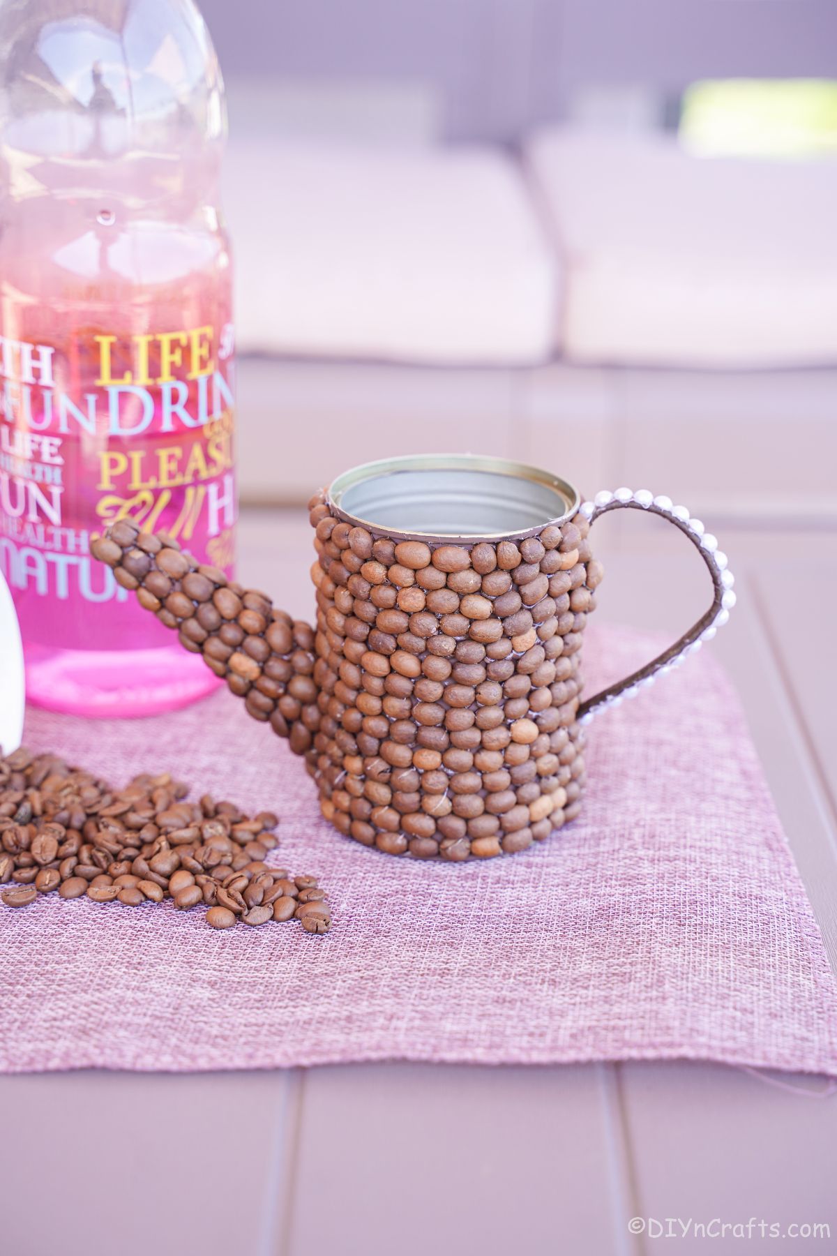 Napperon violet sous l'arrosoir en grains de café par une bouteille colorée rose
