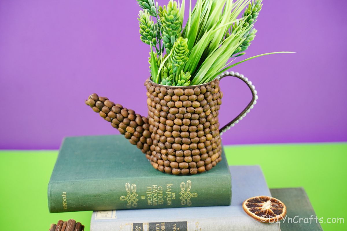 watering can holding flowers on green book with purple background