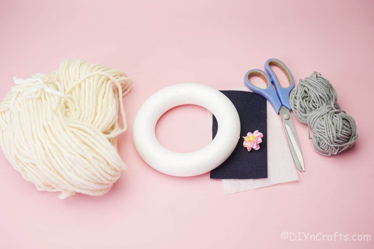 Styrofoam wreath form, yarn, felt, and scissors on pink table