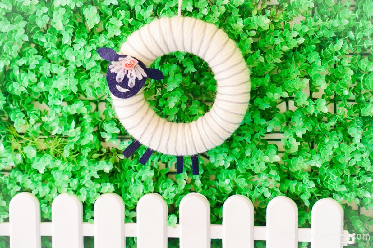 yarn sheep wreath on grass with white picket fence