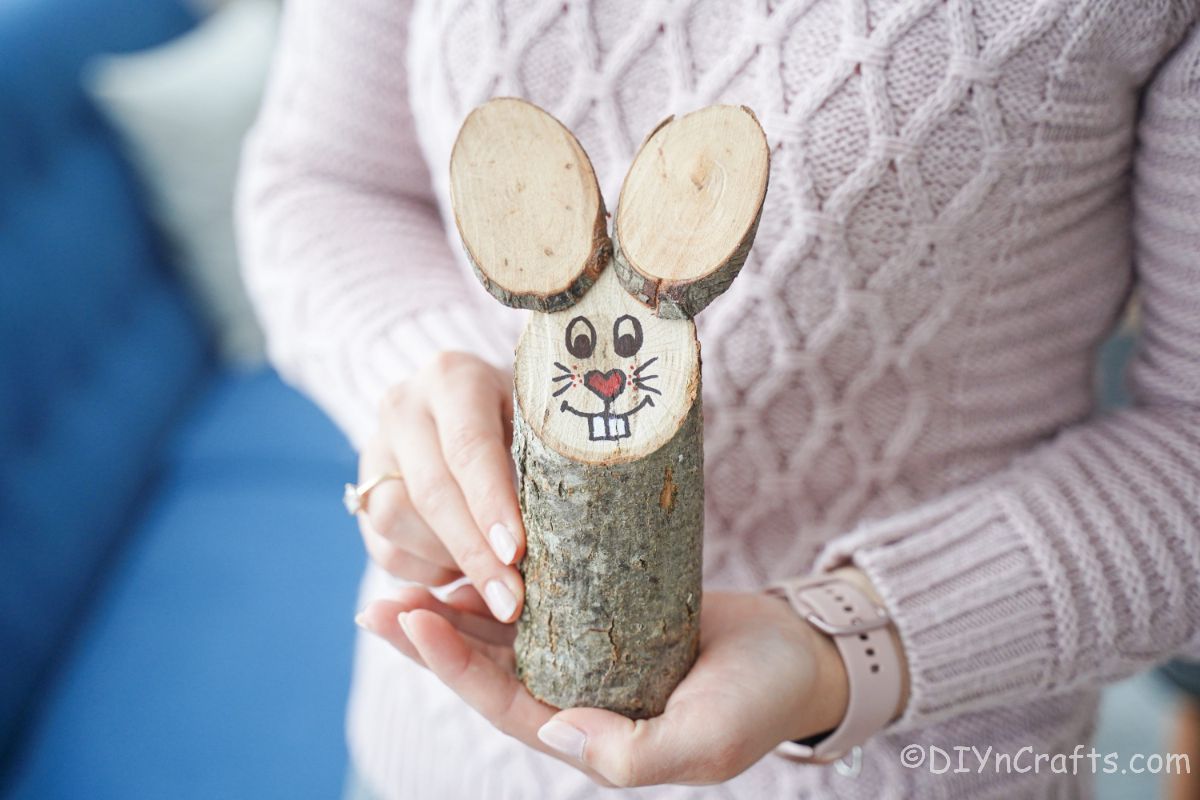 woman in pink sweater with watch holding a log and wood slices that look like a bunny
