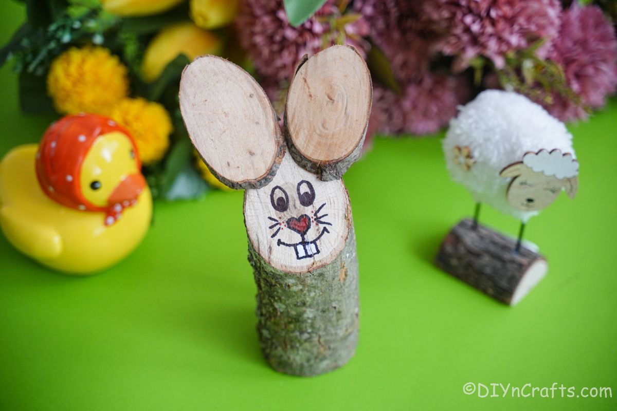 bunny log sur table verte avec des moutons pom pom et des fleurs en arrière-plan