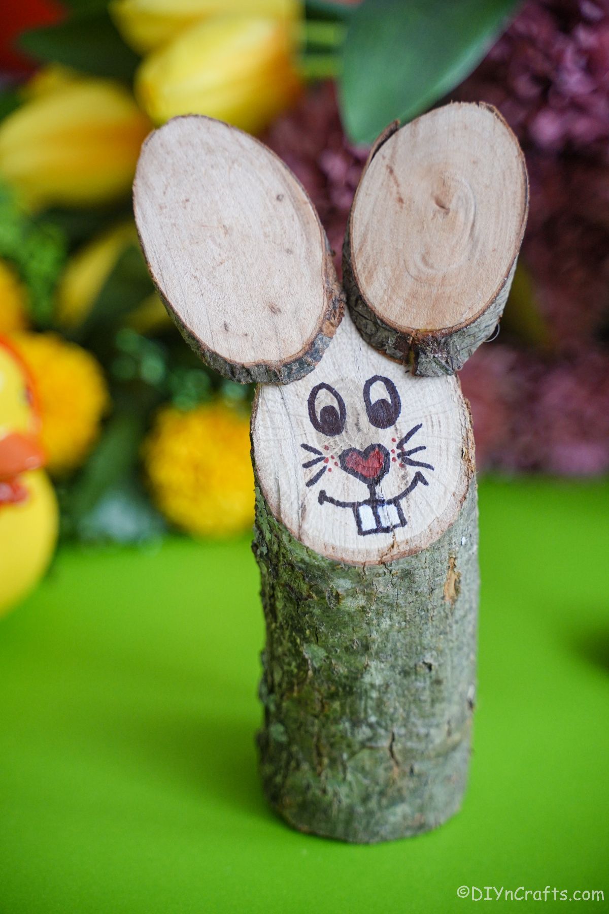bunny made out of a log and wood slices on green table with flowers in background