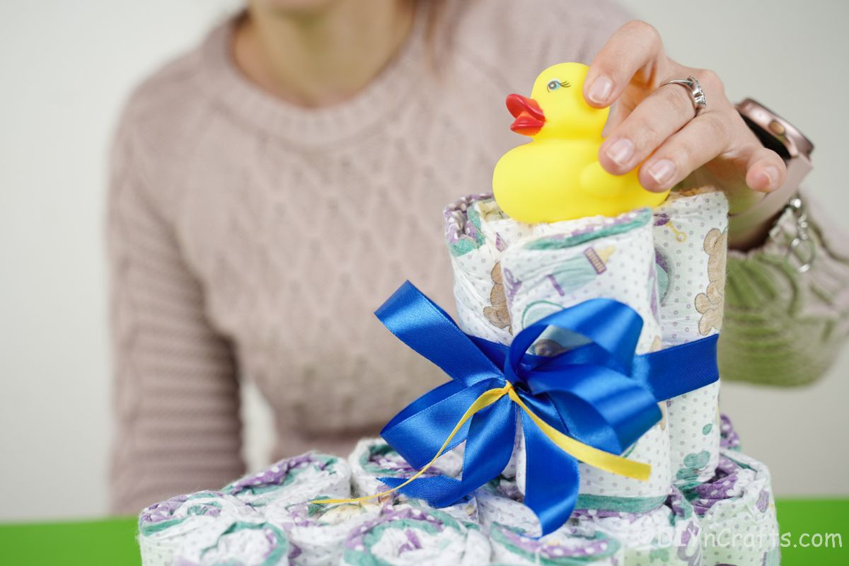 hand putting rubber ducky on top of diaper cake