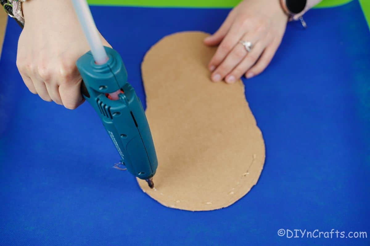 blue glue gun adding glue to cardboard shoe shape on top of blue paper