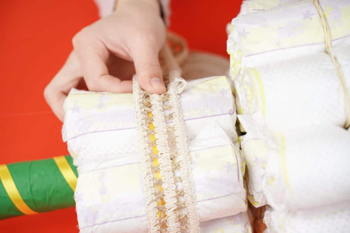 hand gluing lace ribbon onto small bundle of diapers