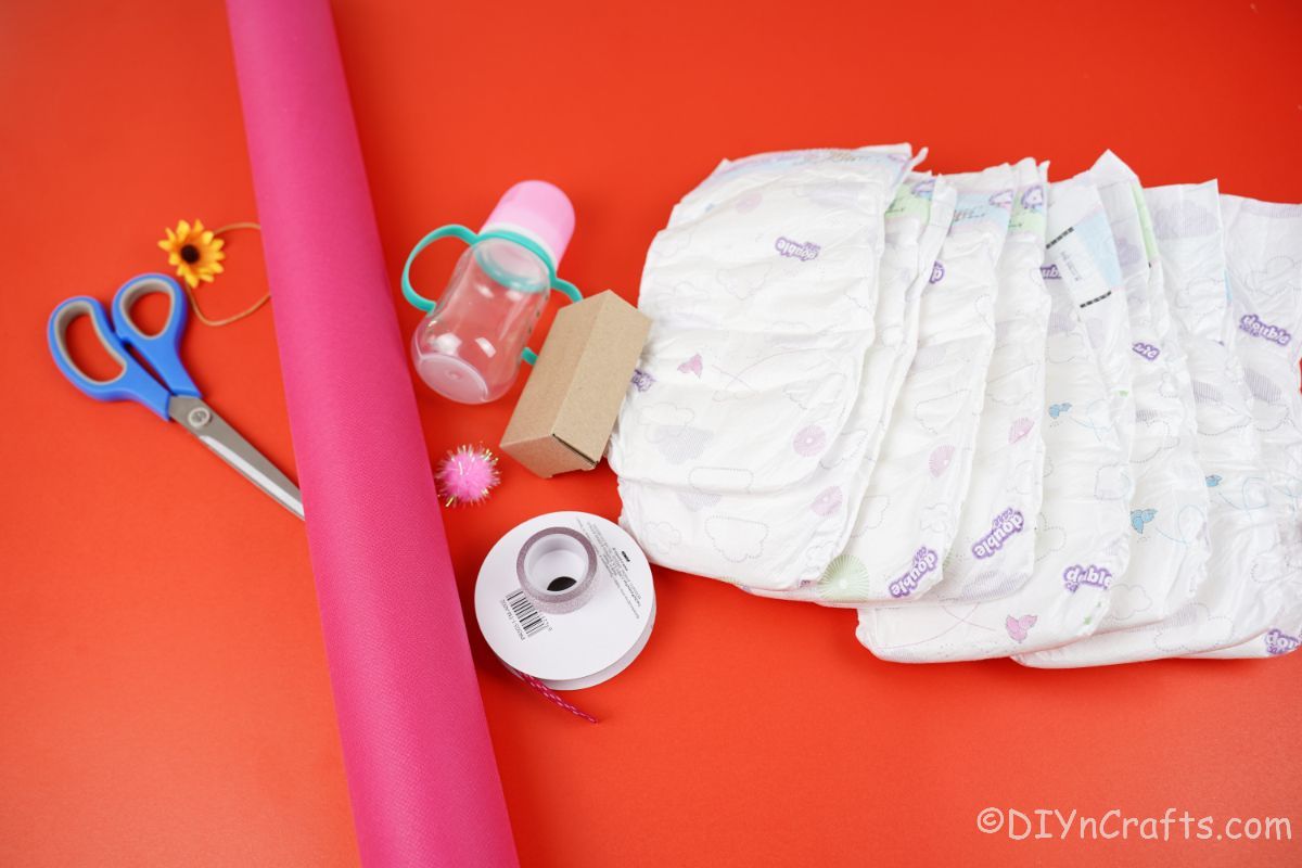 diapers pink paper baby bottle scissors on red table