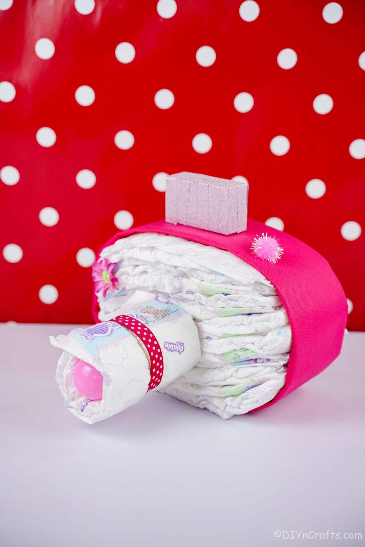 red and white polka dot background behind pink camera diaper cake