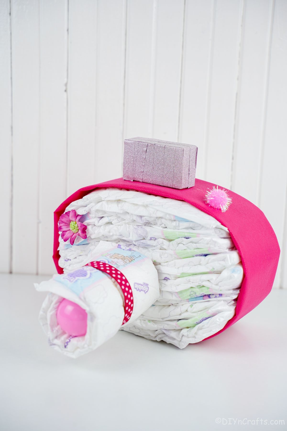 camera diaper cake with pink accents on white table with white paneling background
